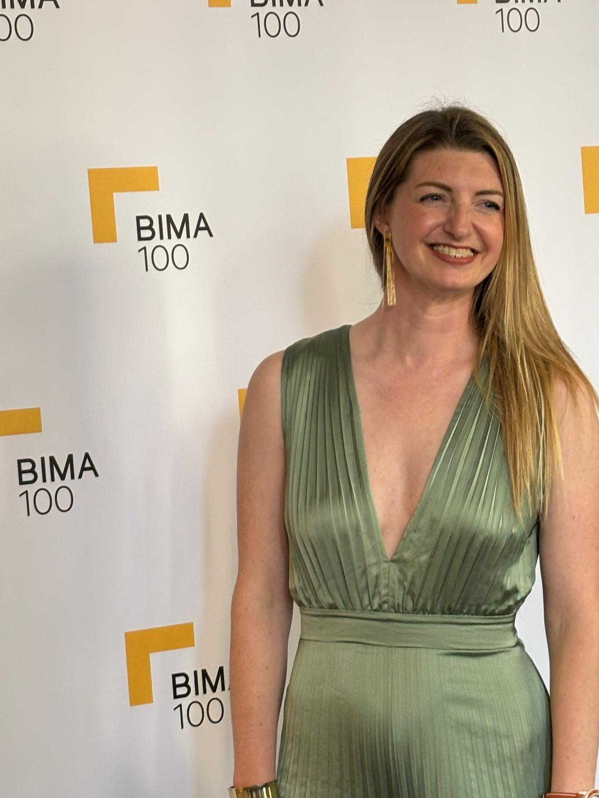 Sarah Levett in front of the BIMA 100 logo wall